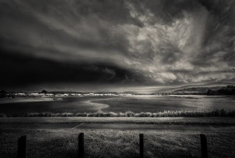Storm clouds loom ominously over a serene lake in a captivating black and white photo.