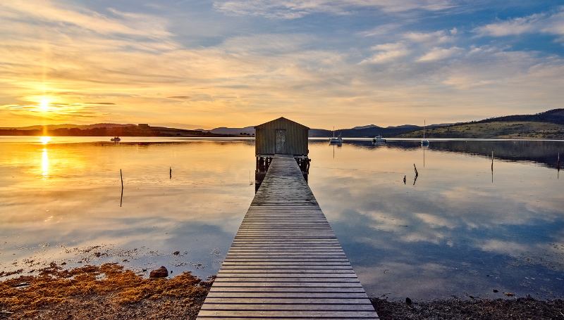 A wooden dock leading to a small house on the water, creating a serene and picturesque scene.