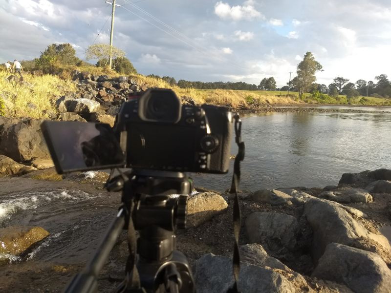 Nikon Camera - A camera on a tripod captures a scenic view of a river, showcasing its serene beauty and tranquil surroundings.