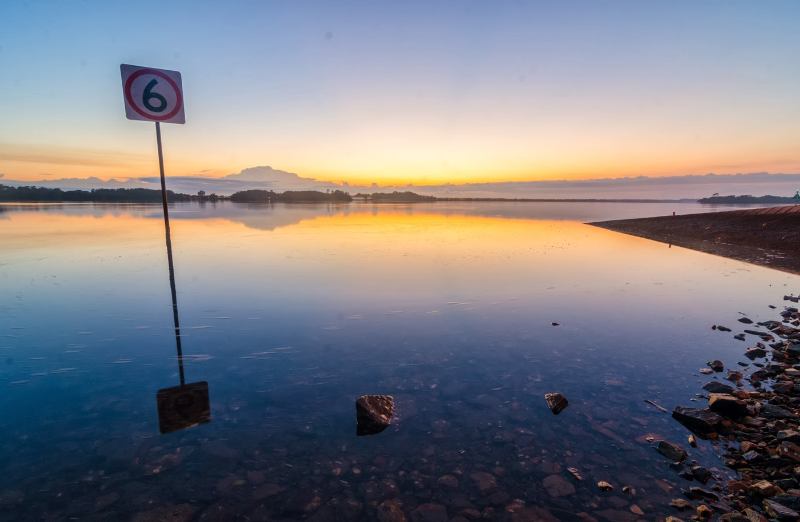 A sign reflecting in the water at sunset, creating a serene and captivating scene.